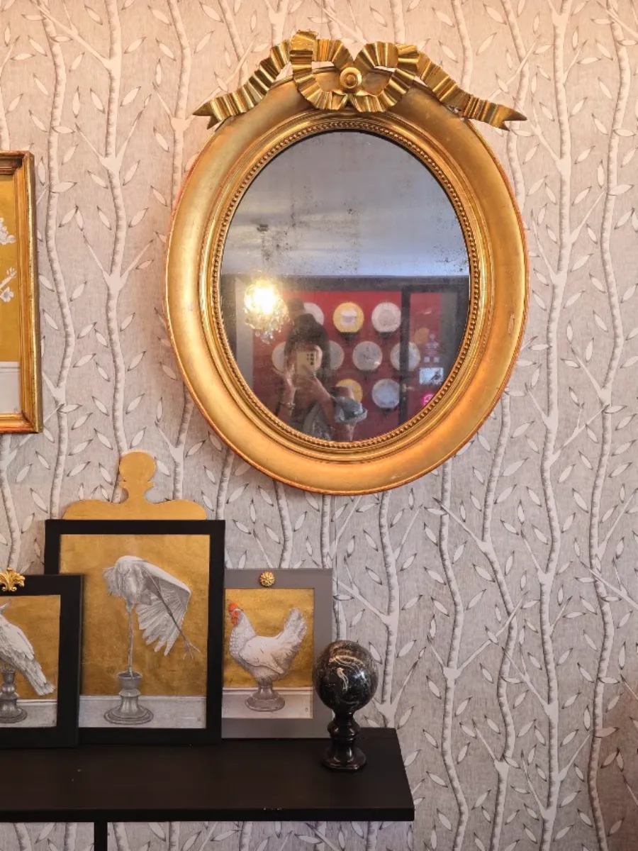 A gilded mirror above framed drawings